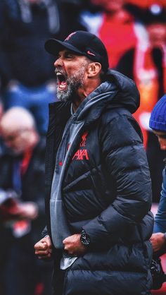 an older man in a black jacket and hat standing on the sidelines with his mouth open