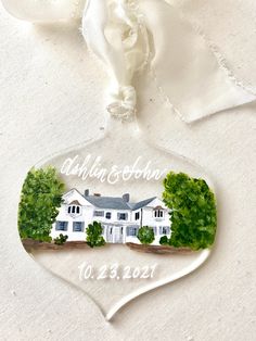 a glass ornament with a white house and trees on the front is shown