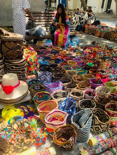 a woman standing in front of a table filled with lots of colorful baskets and hats