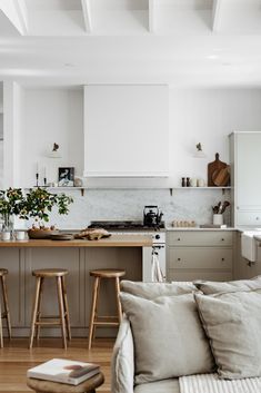 a living room and kitchen area with white walls, wood flooring and wooden stools