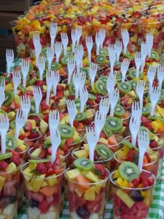 many plastic forks are placed in cups filled with fruit salads and kiwi slices