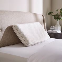 a close up of a bed with a pillow on it and a vase in the background