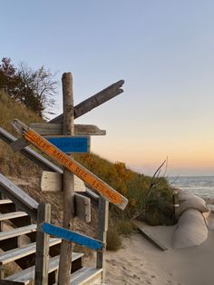 a wooden sign sitting on the side of a sandy beach next to the ocean at sunset