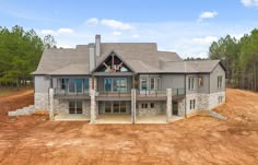 a large house sitting in the middle of a dirt field next to trees and grass