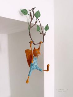 a toy squirrel hanging from a branch with leaves on it's back and feet