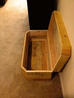 an empty wooden box sitting on the floor next to a black trash can and carpet