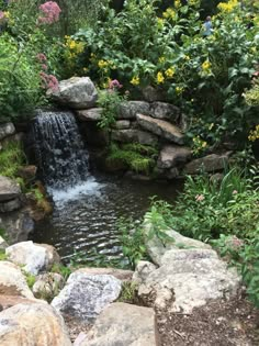 there is a small waterfall in the middle of this garden with rocks and flowers around it