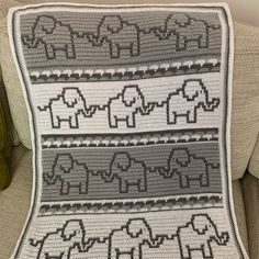 a crocheted afghan with elephants on it sitting on a couch next to a pillow