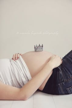 a pregnant woman wearing a tiara laying on the floor with her belly up to her chest