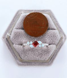 a ring with two stones on it sitting in a velvet box next to a penny