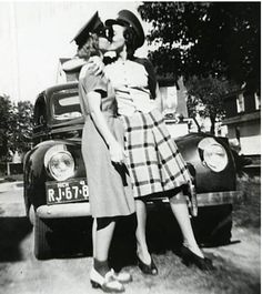 black and white photograph of two women standing next to an old car