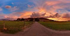 the sun is setting over an open field with a dirt road in front of it