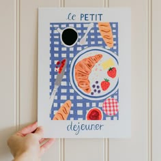 a person holding up a card with food on it that reads le petit dejeuner