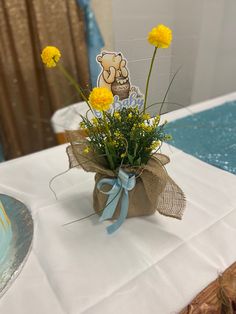 a vase filled with yellow flowers sitting on top of a white tablecloth covered table