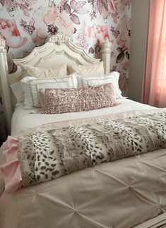 a white bed topped with pillows next to a pink wallpaper covered in floral designs