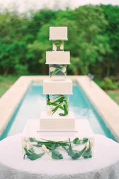 a tall white cake sitting on top of a table next to a pool with greenery