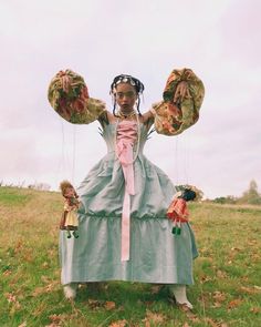 a woman in a blue dress holding two stuffed animals on her shoulders and standing in a field