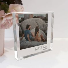 a glass photo frame with a couple sitting on rocks in front of some pink flowers