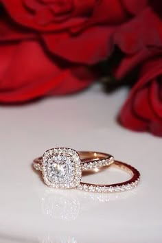 a diamond ring sitting on top of a white surface next to red roses and flowers