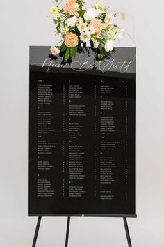 a black and white wedding seating chart with flowers on top is shown in front of a gray background