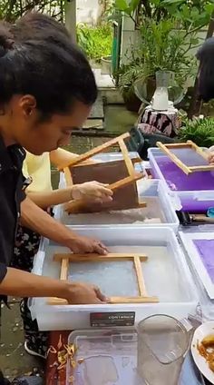 two people working on some kind of art project at an outdoor table with purple and white trays