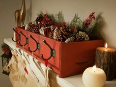 a wooden box filled with pine cones sitting on top of a mantle next to a lit candle