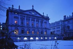 an old building lit up at night with snow on the ground