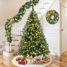 a decorated christmas tree with presents under the banister and stairs in front of it