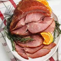 ham with orange slices and rosemary on a white platter next to silver utensils