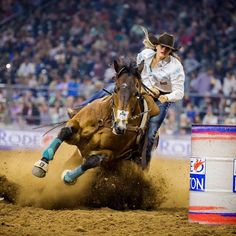 a man riding on the back of a brown horse next to a barrel in an arena