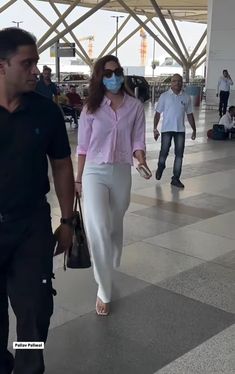 a man and woman walking through an airport wearing face masks to protect them from the sun