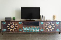 a tv is sitting on top of a wooden entertainment center with an intricately painted design