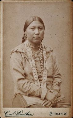 an old black and white photo of a woman in native clothing with beads on her head