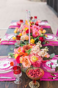 the table is set with pink and yellow flowers, plates, silverware, and candles