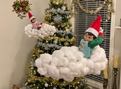 an elf is sitting on top of a cloud in front of a christmas tree