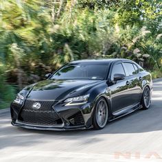 a black sports car driving down the road with trees in the backgrouund