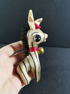 a hand holding a small toy horse in it's right hand, with a red ribbon around its neck