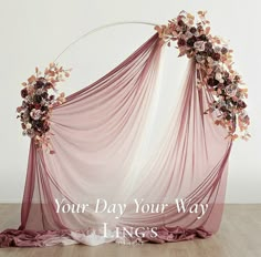 an arrangement of flowers and sheer fabric draped over a wooden floor in front of a white wall