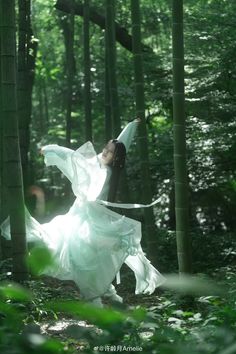 a woman in a white dress is dancing in the woods