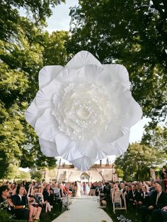 a large white flower hanging from the side of a tree in front of a wedding ceremony