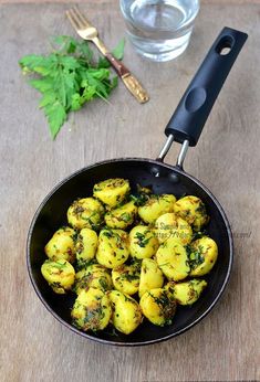 a pan filled with cooked potatoes on top of a wooden table next to a glass of water