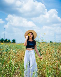 a woman standing in a field holding a sunflower up to her face while wearing a straw hat