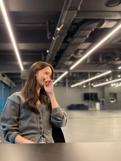 a woman sitting at a table talking on her cell phone in an empty room with lights overhead