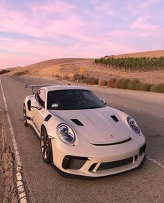 a white sports car is parked on the side of the road in front of some hills