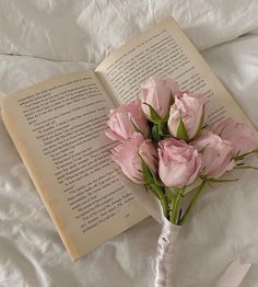 a bouquet of pink flowers sitting next to an open book on top of a bed