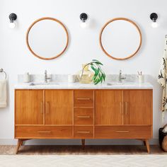 two round mirrors are above the double sink vanity in this bathroom with wood cabinets and white walls