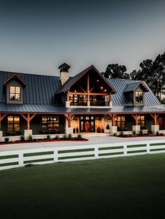 a large house with a white fence and green grass in the front yard at night