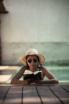 a woman wearing sunglasses and a straw hat is laying on the ground reading a book