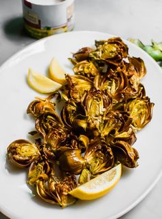 a white plate topped with artichokes next to lemon wedges and a jar of mayonnaise