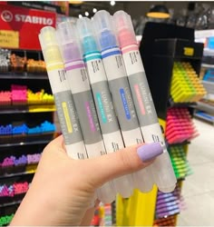 a person holding three markers in front of a store display filled with different colored pens